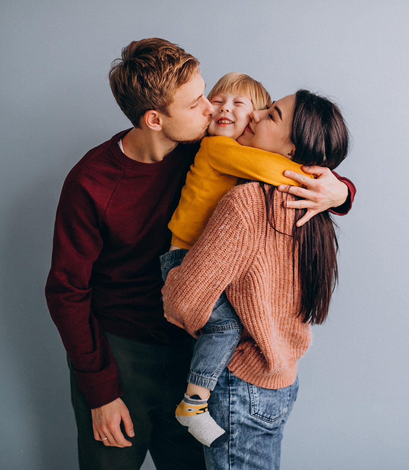 Family of three hugging and kissing child in yellow sweater