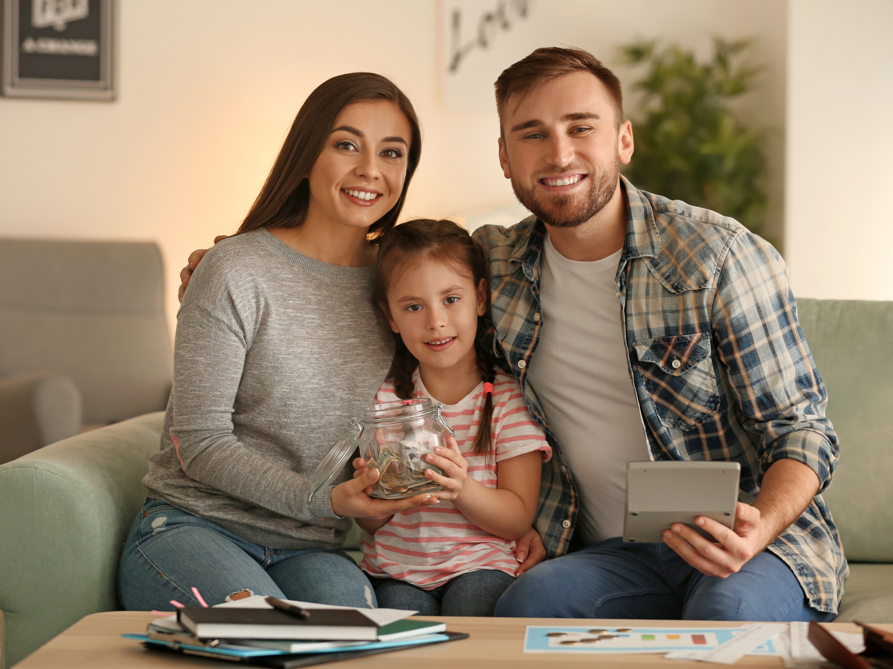 Family of three saving money together, smiling on comfortable couch