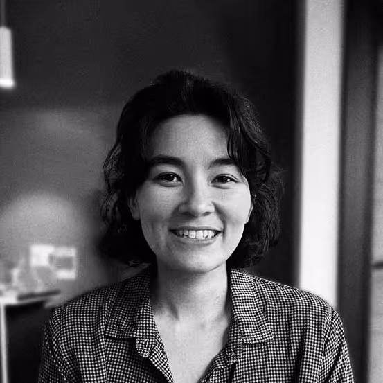 Smiling woman with short dark hair wearing a checkered shirt in a softly lit room.
