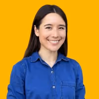 Smiling woman with long dark hair wearing a blue button-up shirt against a yellow background.