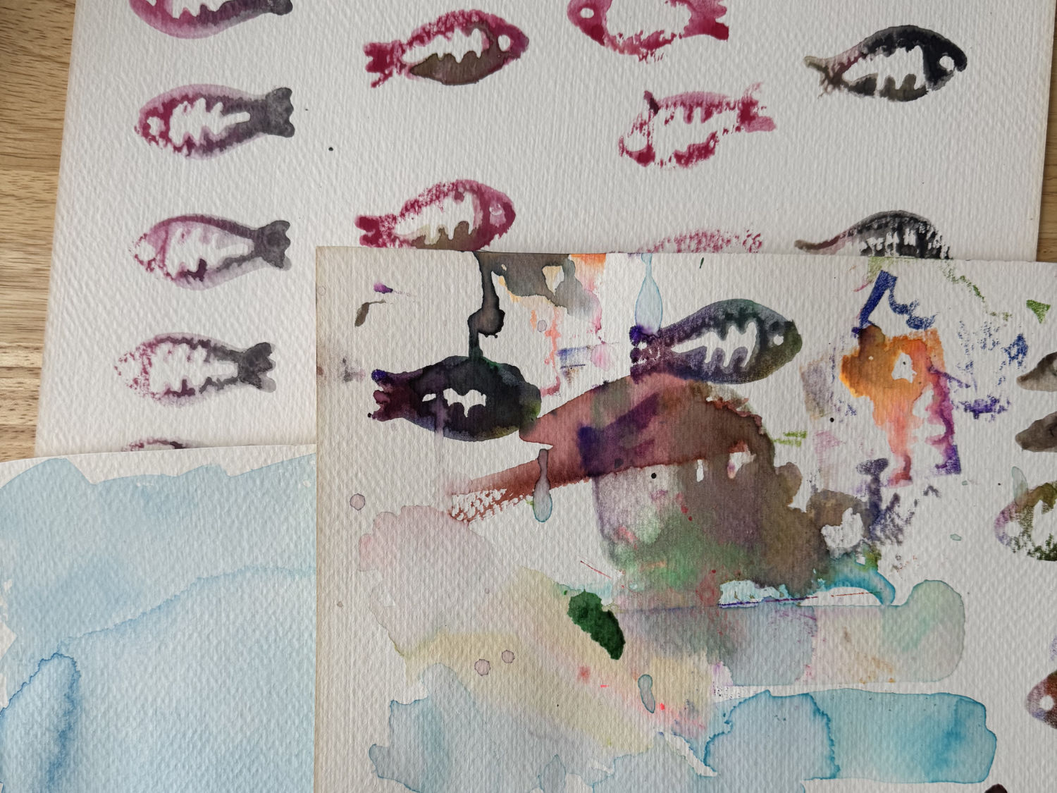 Three pieces of paper with fish-shaped stamps made with watercolor paint.