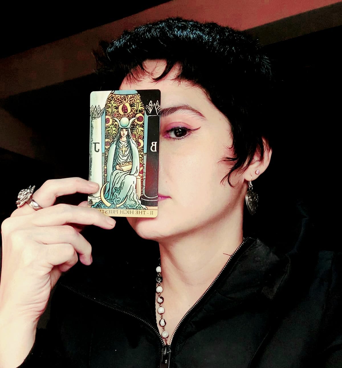 Sabrina Taro, Wiccan tarot reader, posing with the High Priestess card over her right eye as a sacred symbol of insight.