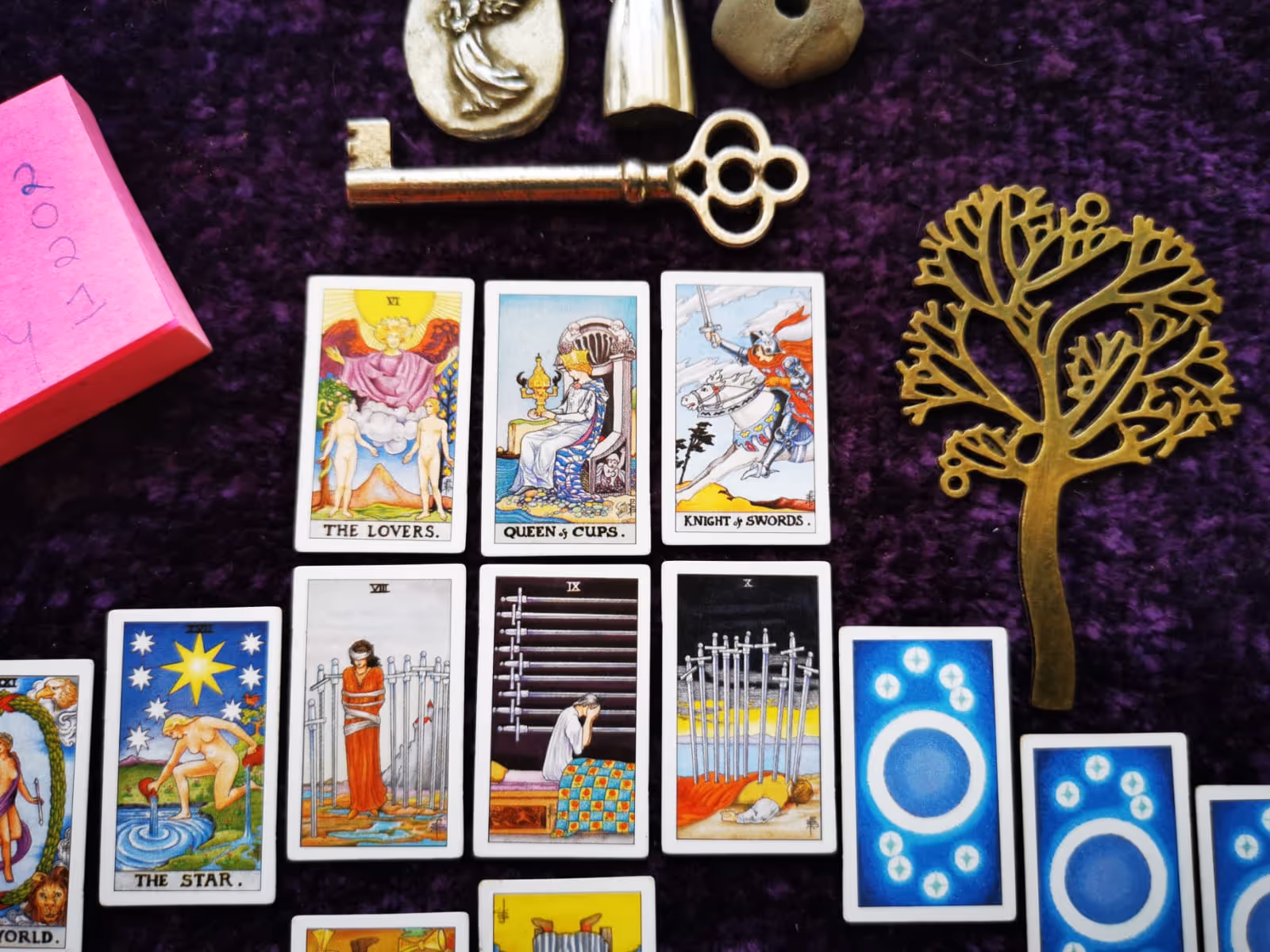 Tiny tarot cards in a hanger-shaped spread with keys, witch stones, angel figurines, and Tree of Life symbol in a Wiccan setup.