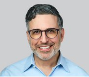 A man wearing glasses and a blue shirt smiles warmly at the camera.