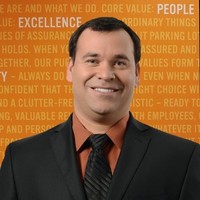 A man in a suit and tie stands confidently against a vibrant orange background.
