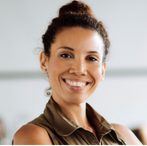 A woman smiling while seated at her desk in a bright office environment.