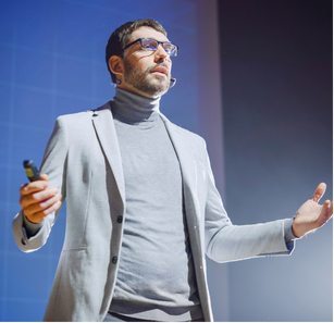 A man in a suit stands at a podium, delivering a presentation to an audience.