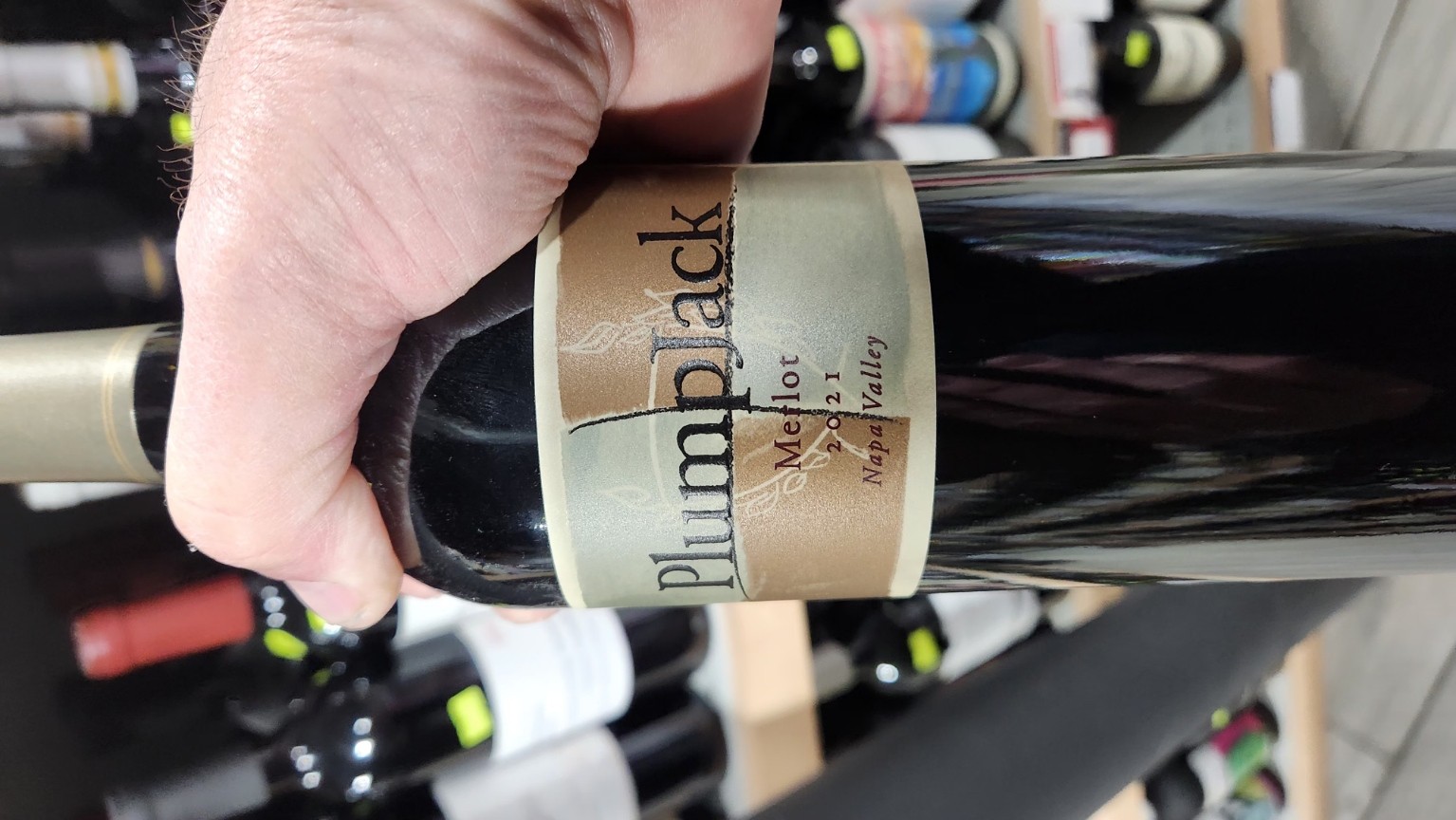 Bottle of PlumpJack Merlot 2021 Napa Valley held in hand among wine, reflecting rich red tones and gold label.