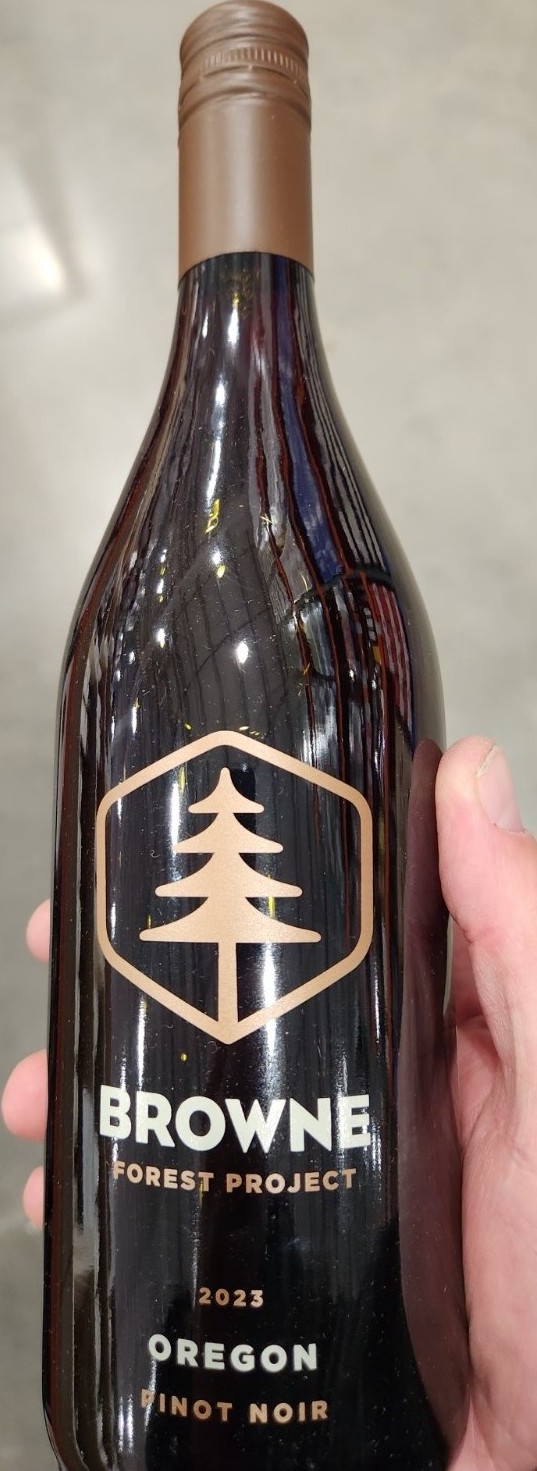 Bottle of 2023 Browne Forest Project Pinot Noir held in hand at a wine store. Oregon Pinot Noir with brown and gold tree logo.