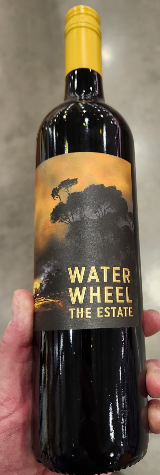 Bottle of Water Wheel Shiraz held in hand, showing the dark label with silhouetted trees and yellow capsule.