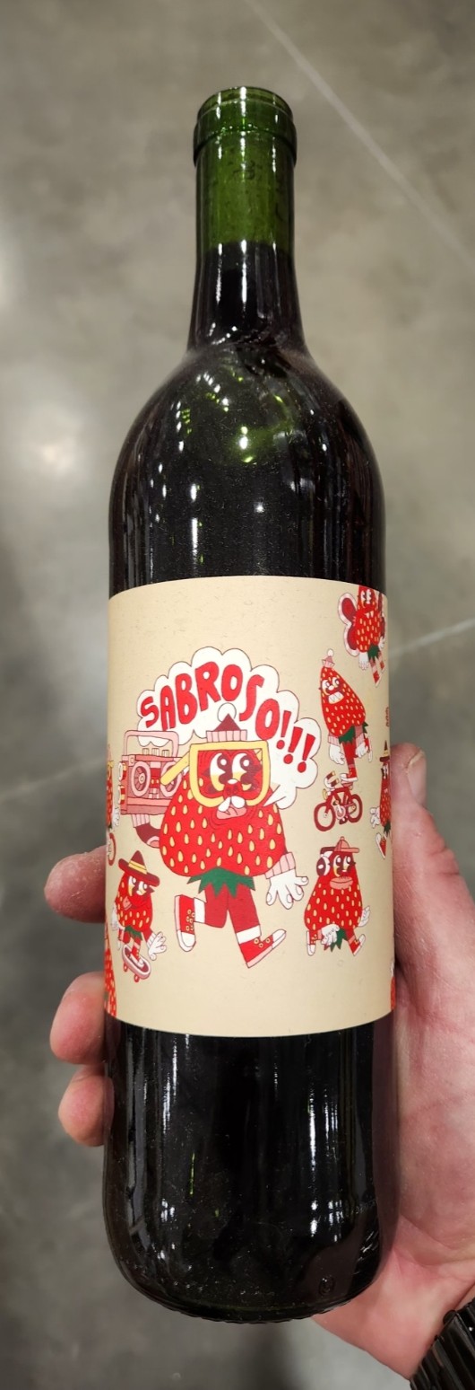 Bottle of Sabroso Red Blend California wine with playful illustrated label, photographed in hand inside a wine store.