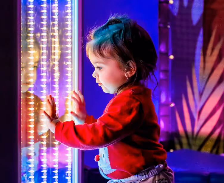 Child in red sweater touching colorful light installation with wonder