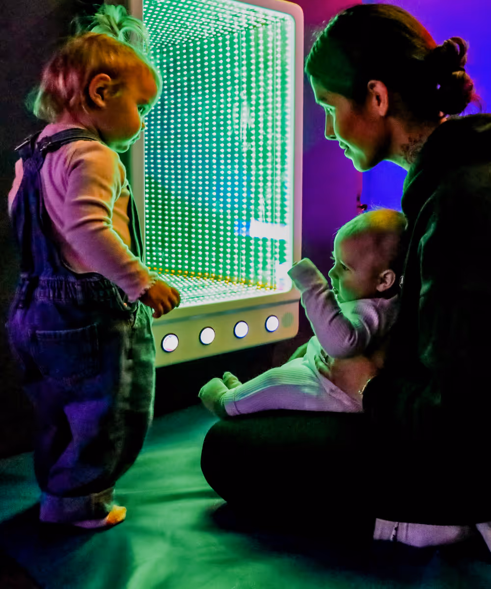 Children exploring interactive green light display with caregiver