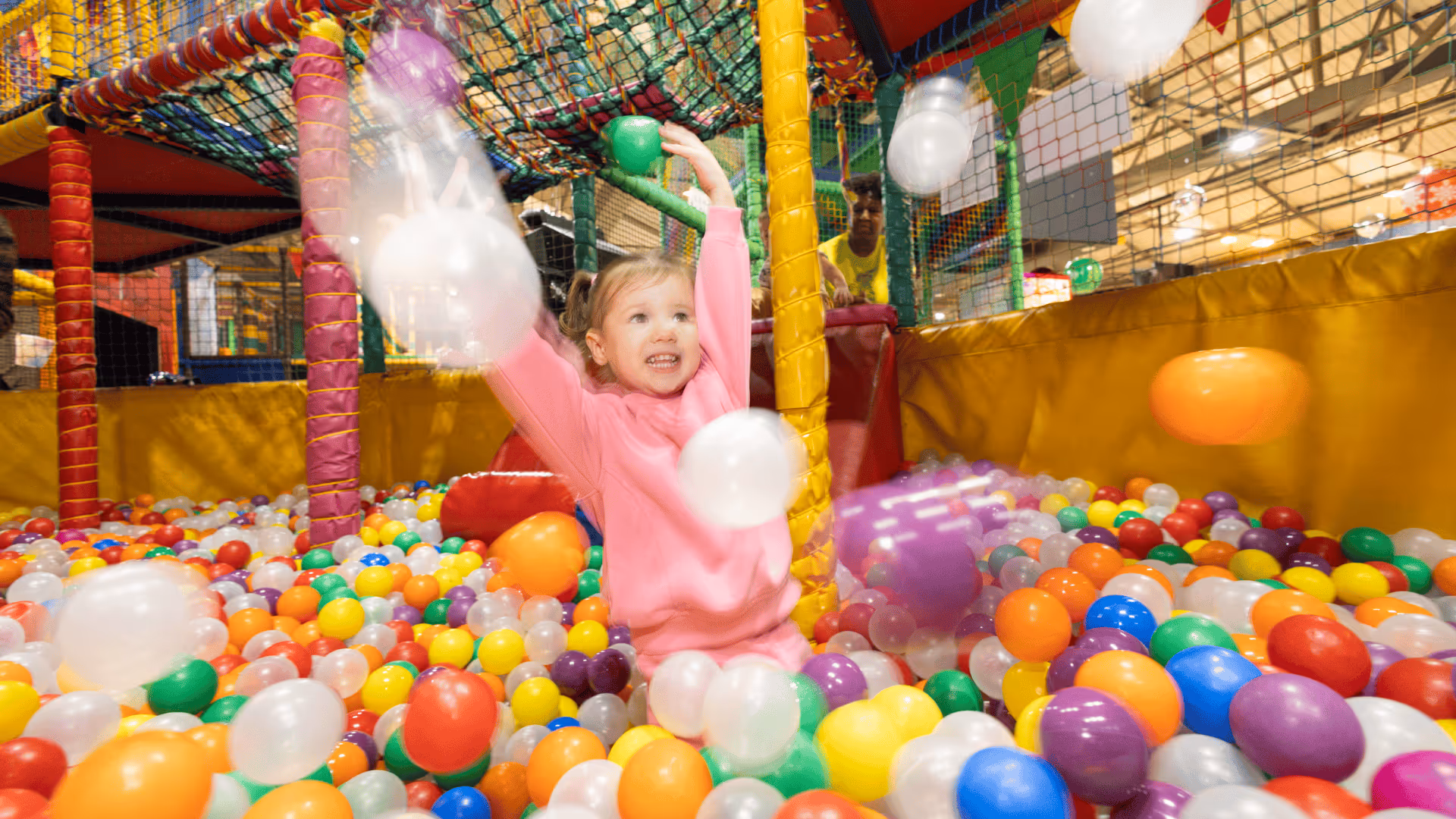 Excited child playing in colorful ball pit, throwing balls with joy