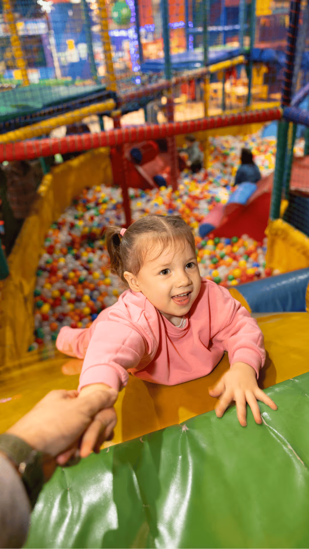 Smiling child in pink sweater playing in colorful ball pit playground
