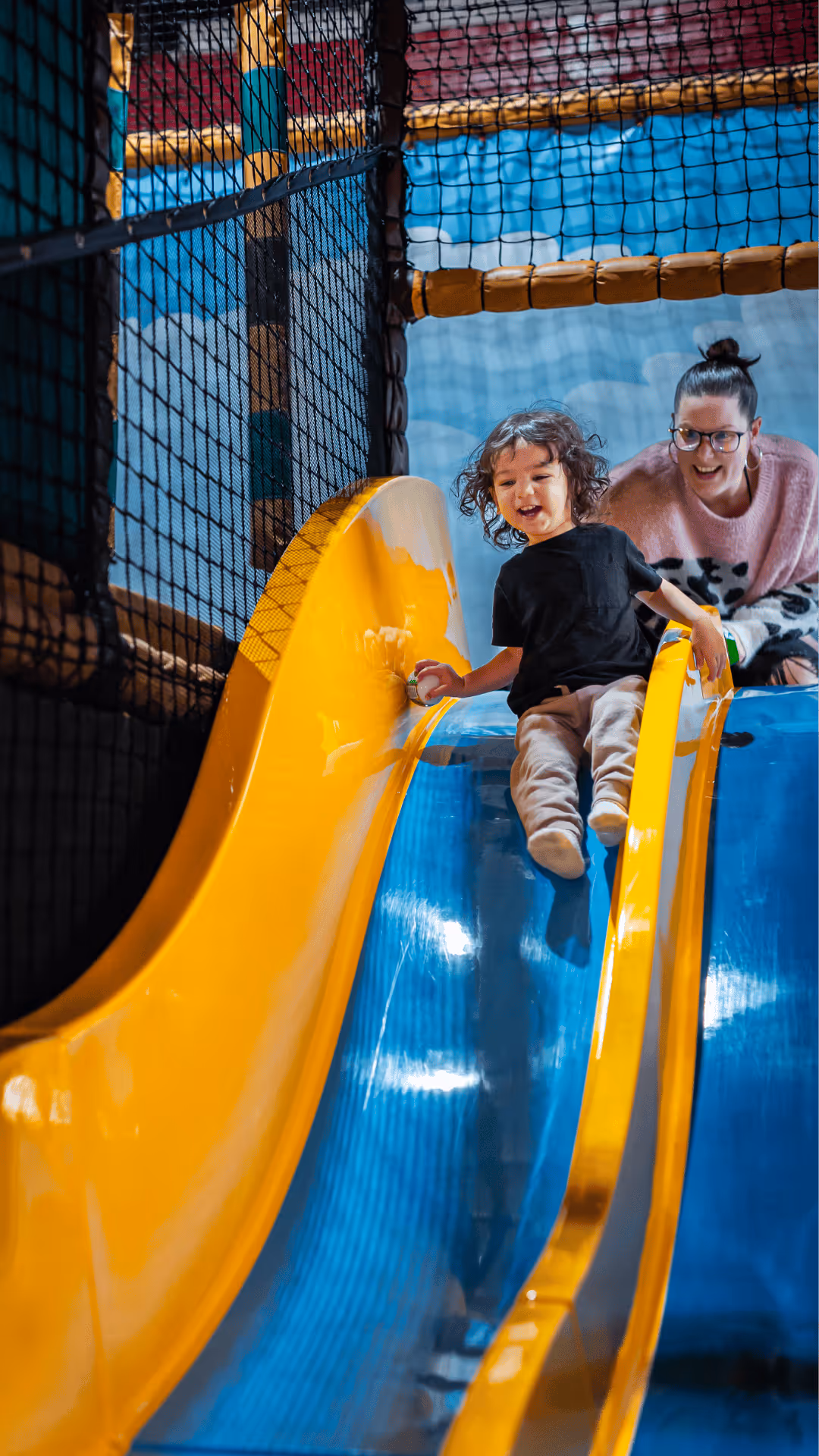 Excited child sliding down a bright yellow and blue playground slide