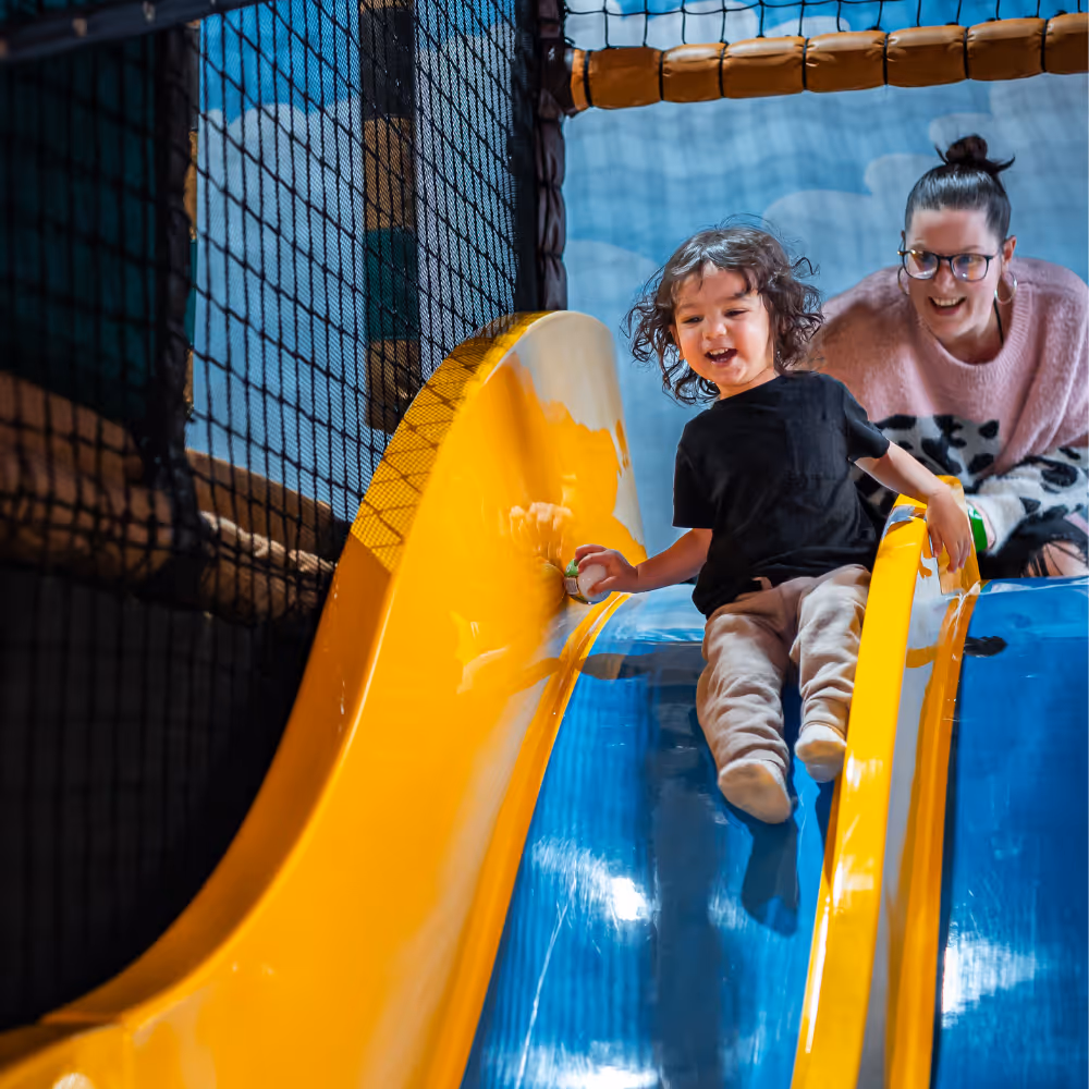 Child sliding down bright yellow slide with joyful expression in play area