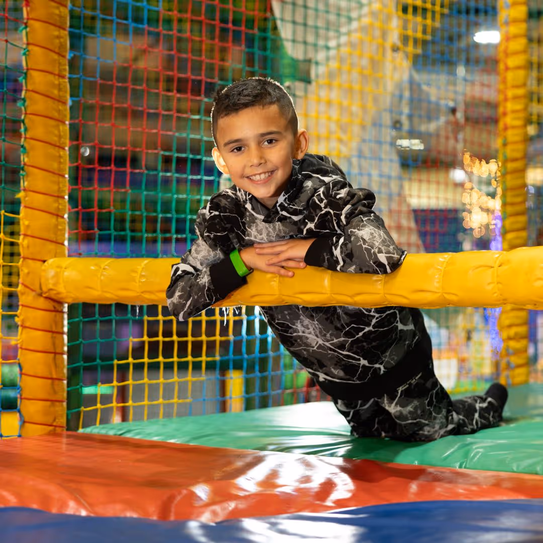 Smiling child leaning on yellow bar in colorful indoor playground