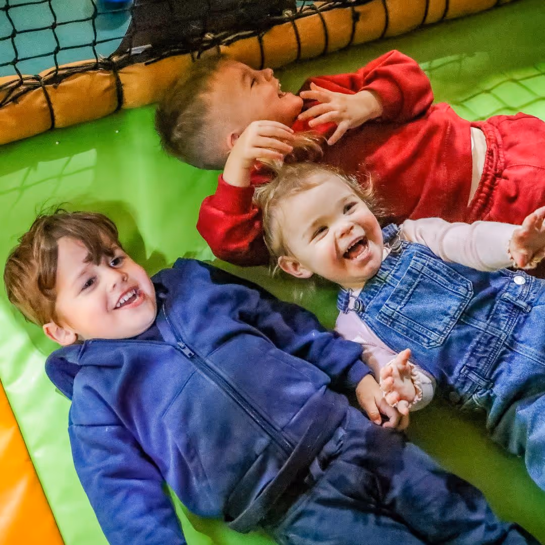 Three children laughing and playing together on a green cushioned surface