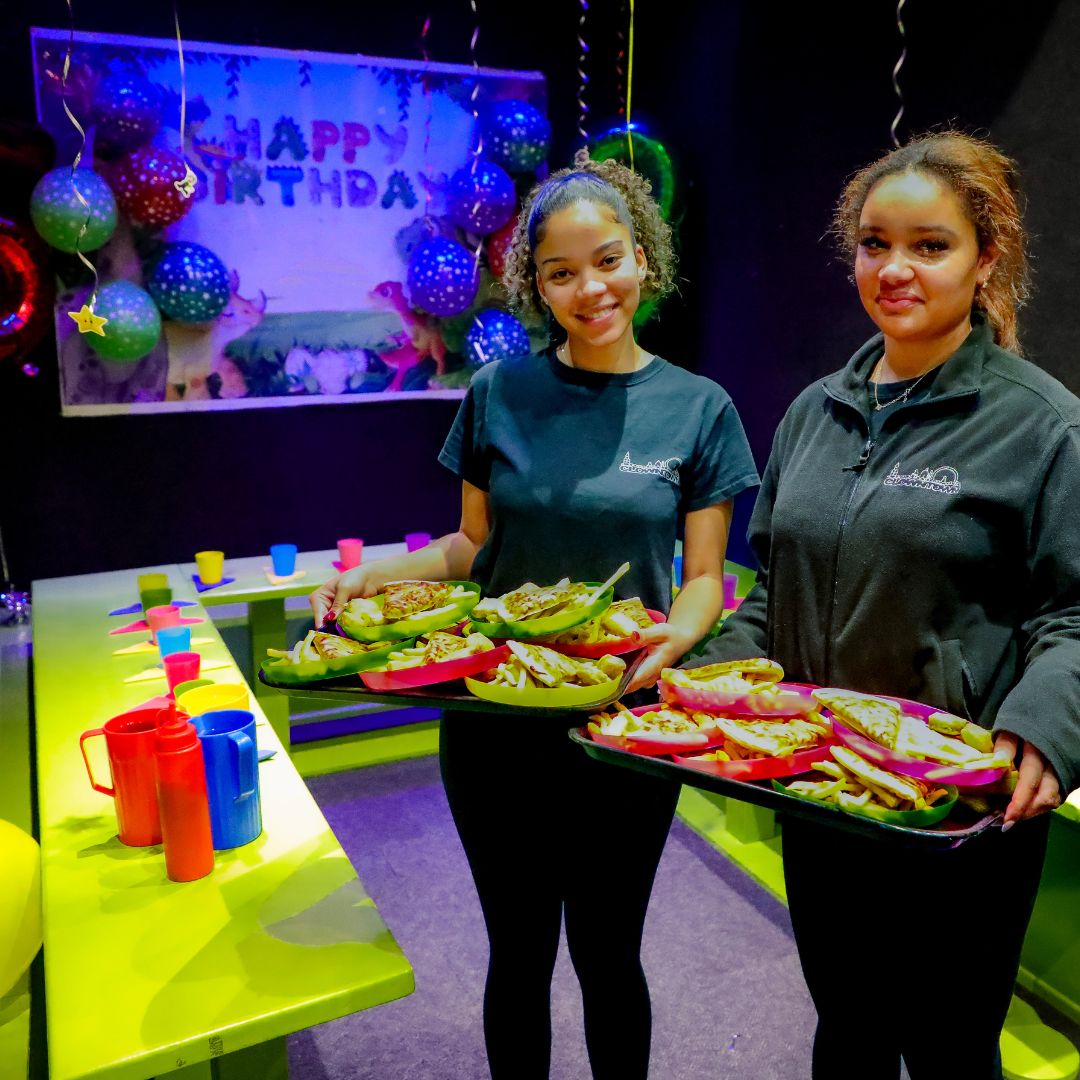 Two staff members holding party food smiling whilst servinf