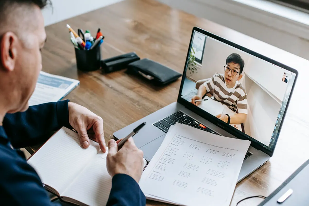An online tutor teaches a student through a video call, working on their laptop during the one-on-one session.