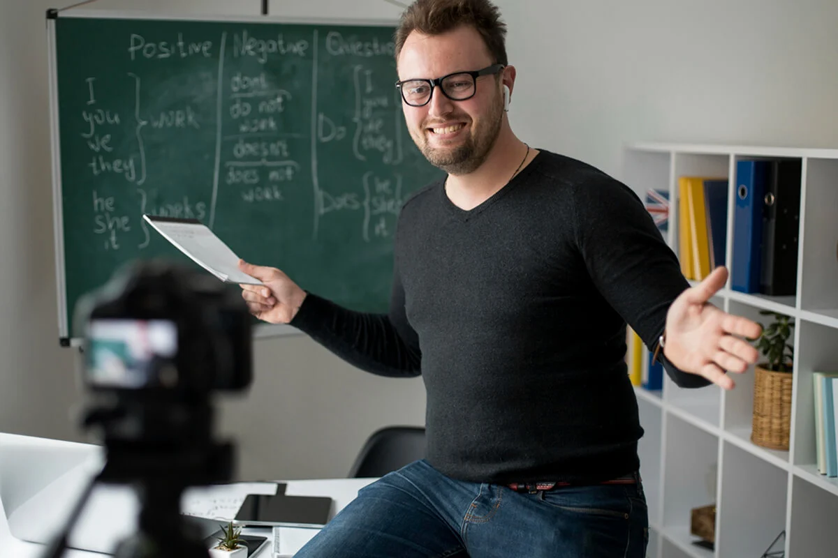 A cheerful tutor wearing glasses conducting an online tutoring session with his students.
