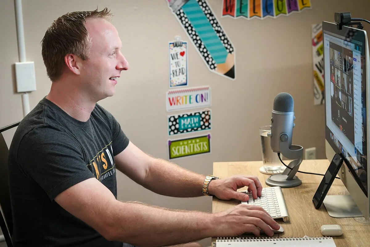 A tutor is teaching a group of students online via a Zoom call through his computer. 