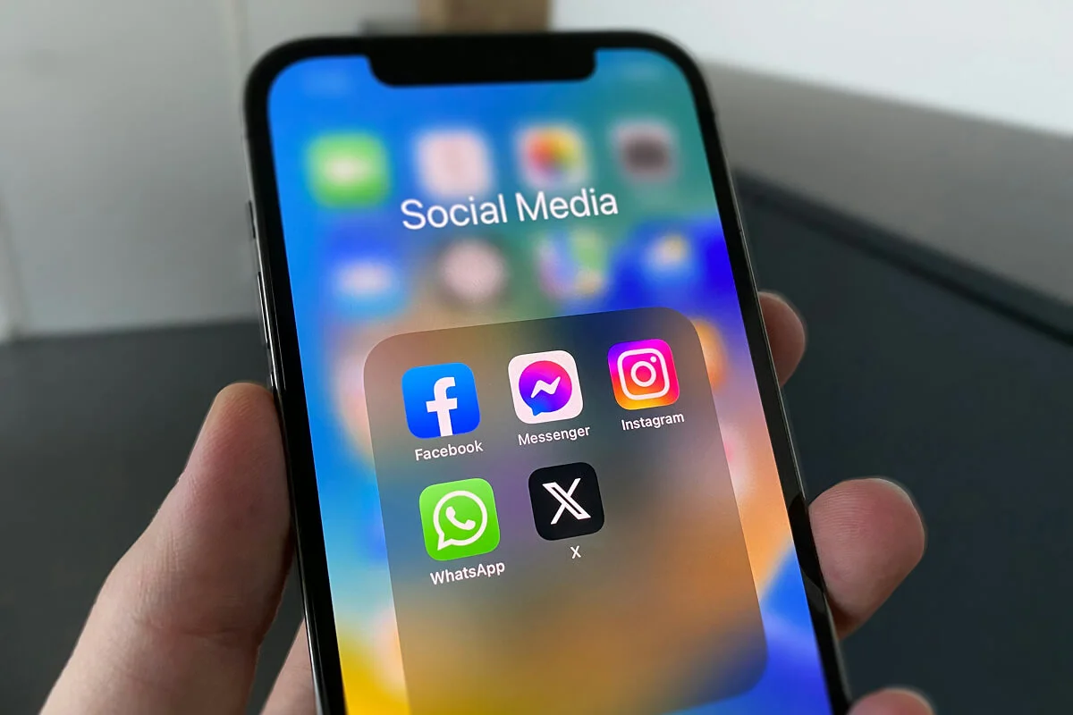 A person holding an iPhone displaying Social Media Apps, including Facebook, Instagram, Messenger, WhatsApp, and X (formerly Twitter).