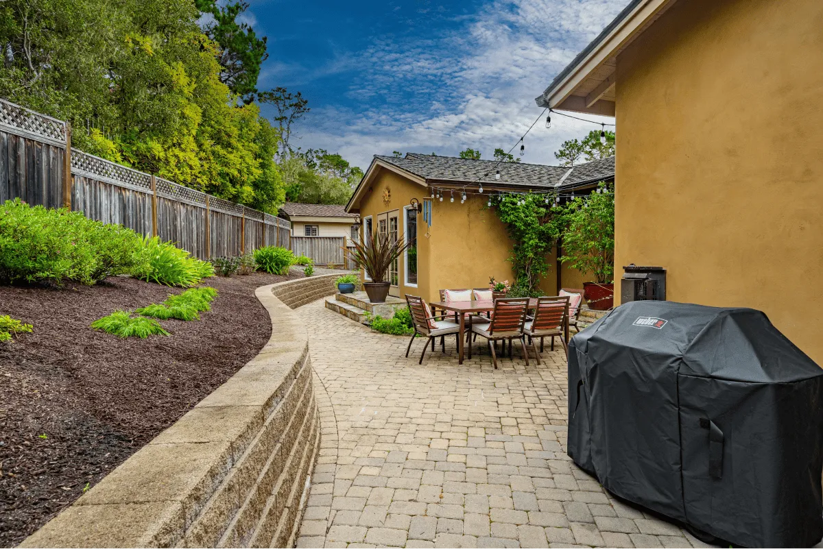 A long view of the wide backyard with the grill and outdoor dining area in view.