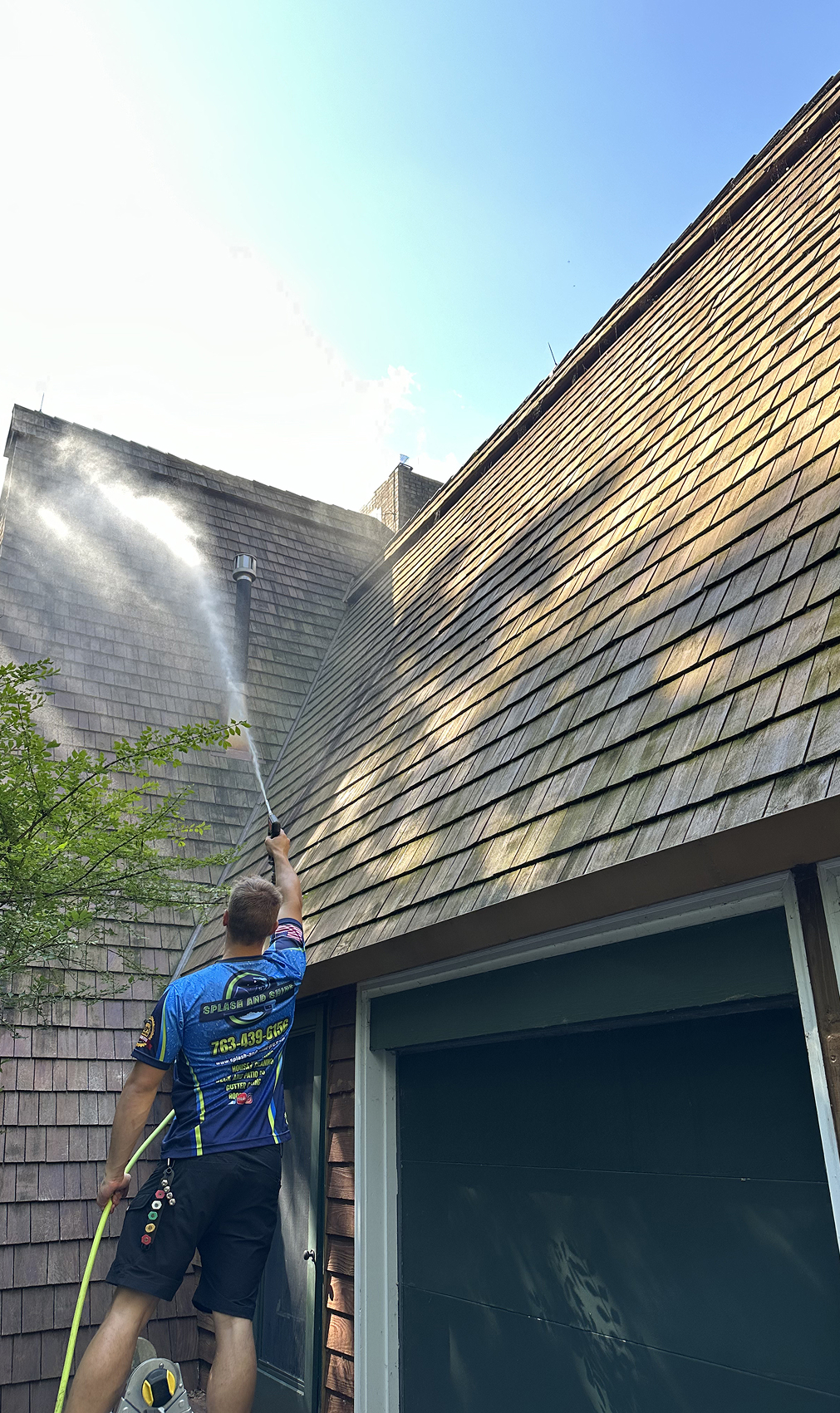 Splash & Shine crew soft washing a roof to remove moss, algae, and black streaks