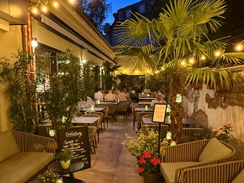 Gemütliche Außenrestaurant-Terrasse bei Nacht mit Gartendekor und Gästen am Tisch.