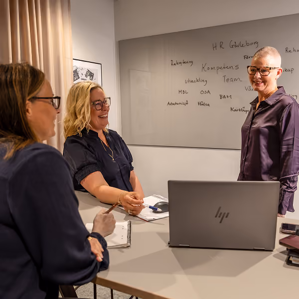 Fyra kollegor samlade runt en datorskärm i ett modernt kontorslandskap med öppen planlösning.