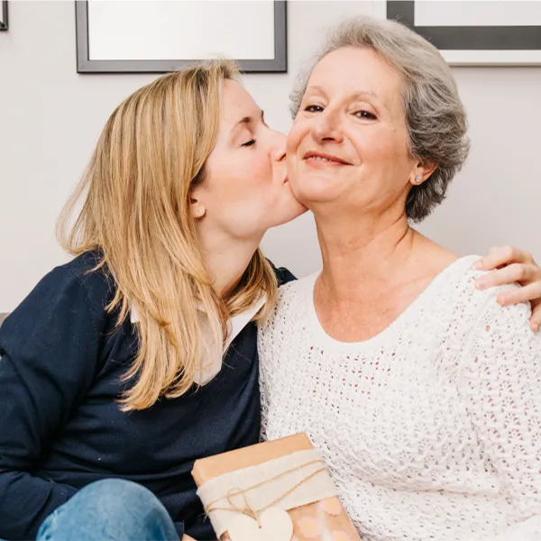 Fiatal nő megpuszilja az édesanyját, kezében egy Rajzkönyvet tartva ajándékként.