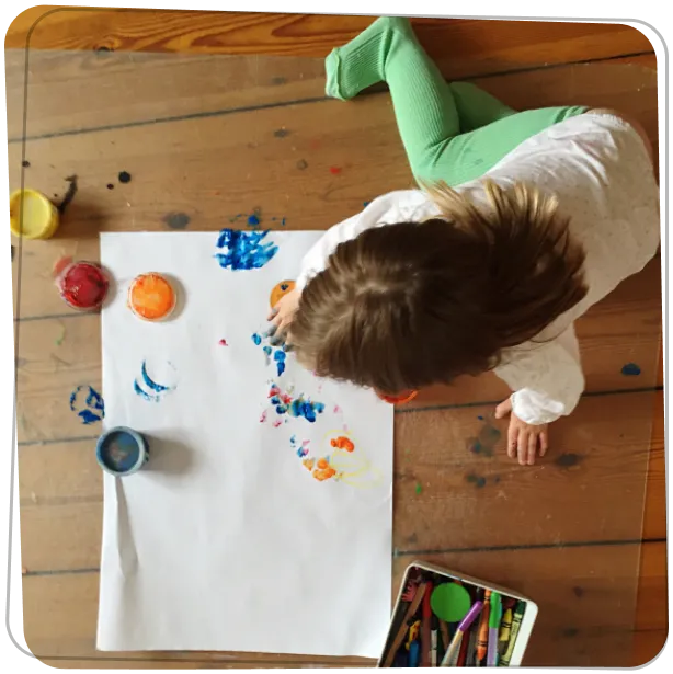 Gyermek felülről nézve festékkel dolgozik a padlón