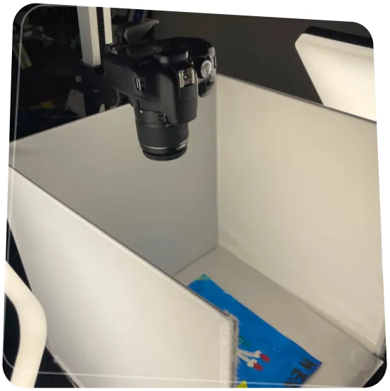 Fényképezőgép felülről fotózza a gyerekrajzokat egy digitalizáló állomáson.