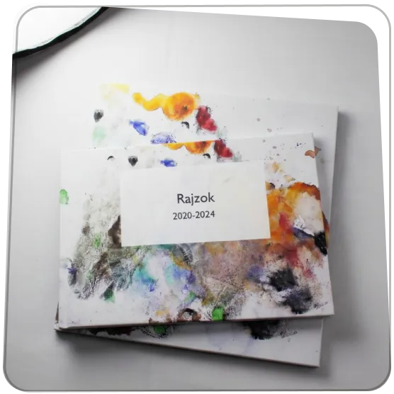 Három különböző méretű Rajzkönyv példány egymásra helyezve az asztalon, színes gyerekrajzok borítóval.