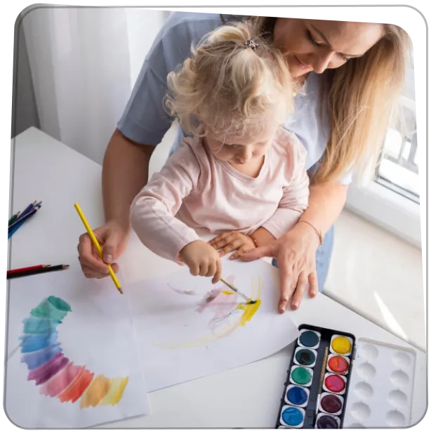 Édesanya és kislánya közösen rajzolnak az asztalnál vízfestékkel, kiválasztják a kedvenc rajzokat a Rajzkönyvhöz.