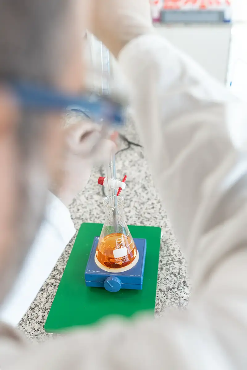 Ein Mann in weißem Kittel und Schutzbrille mischt eine orangene Flüssigkeit in einem Reagenzglas