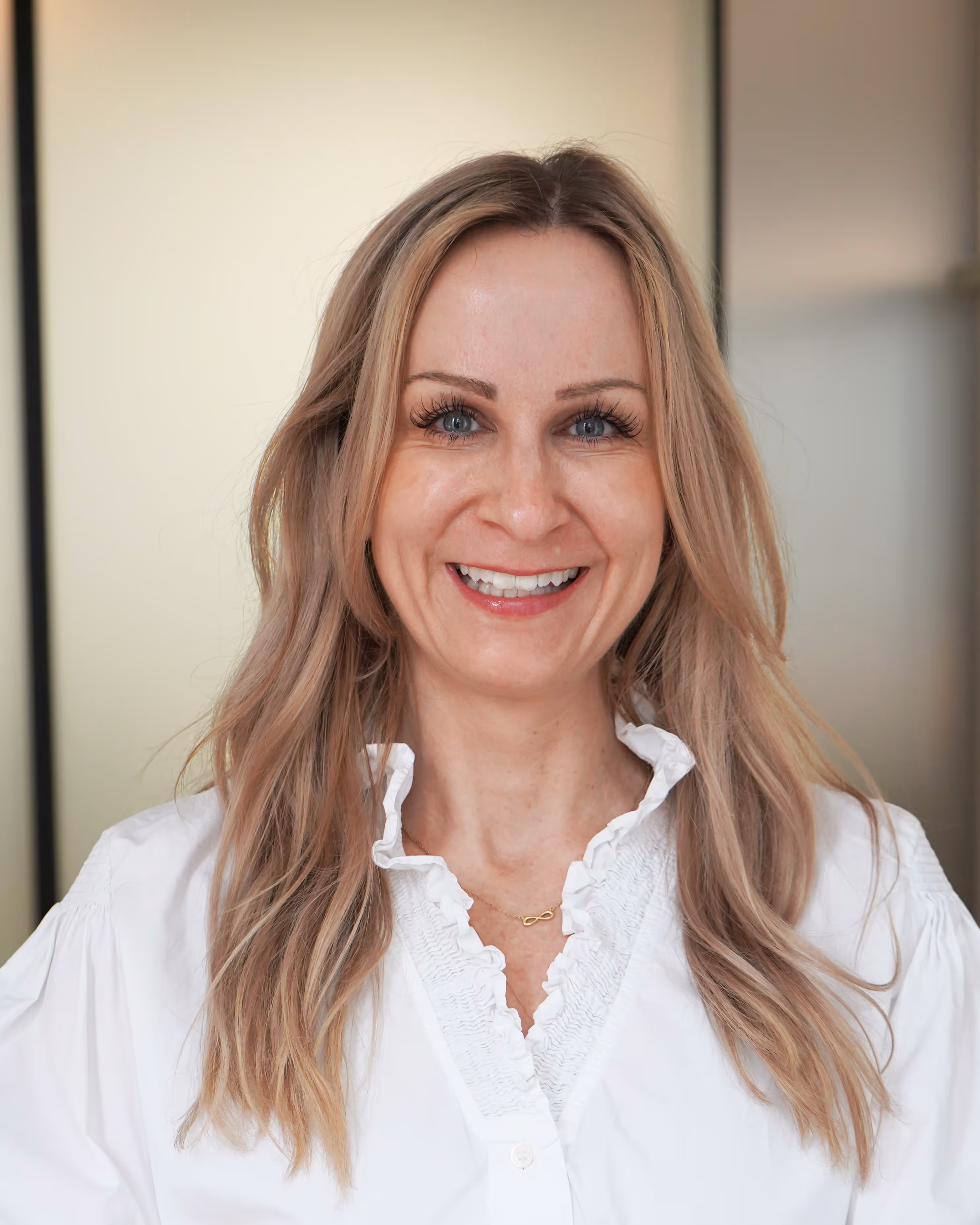 Kirsten Skopp mit langen blonden Haaren und weißer Bluse vor unscharfem Hintergrund.