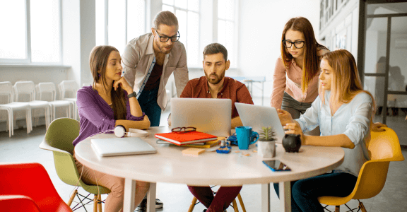 A group of people sitting around a table looking at a laptop.