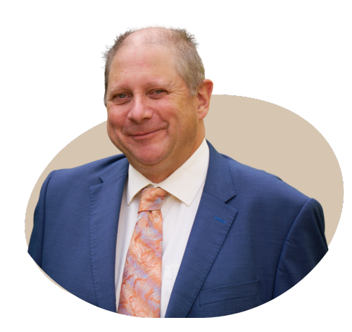 A professional portrait of the director of a private medical insurance brokerage, dressed in a business suit, standing in a modern office setting with a confident and approachable expression.
