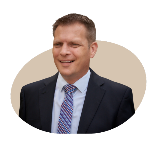 A professional portrait of the director of a private medical insurance brokerage, dressed in a business suit, standing in a modern office setting with a confident and approachable expression.