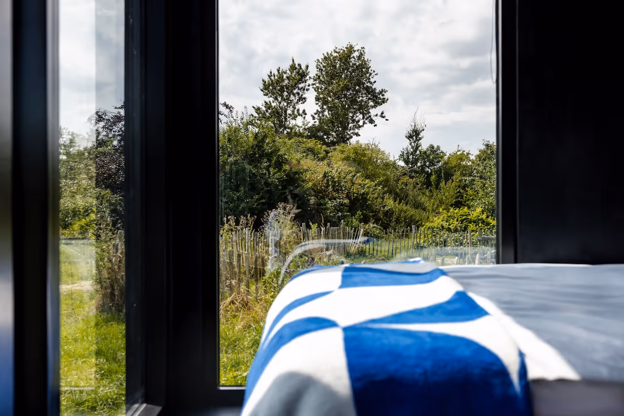 Toller Ausblick aus dem Panoramafenster in die Natur. NORI Cabin auf Rügen mit Decke auf dem Bett von noo.ma