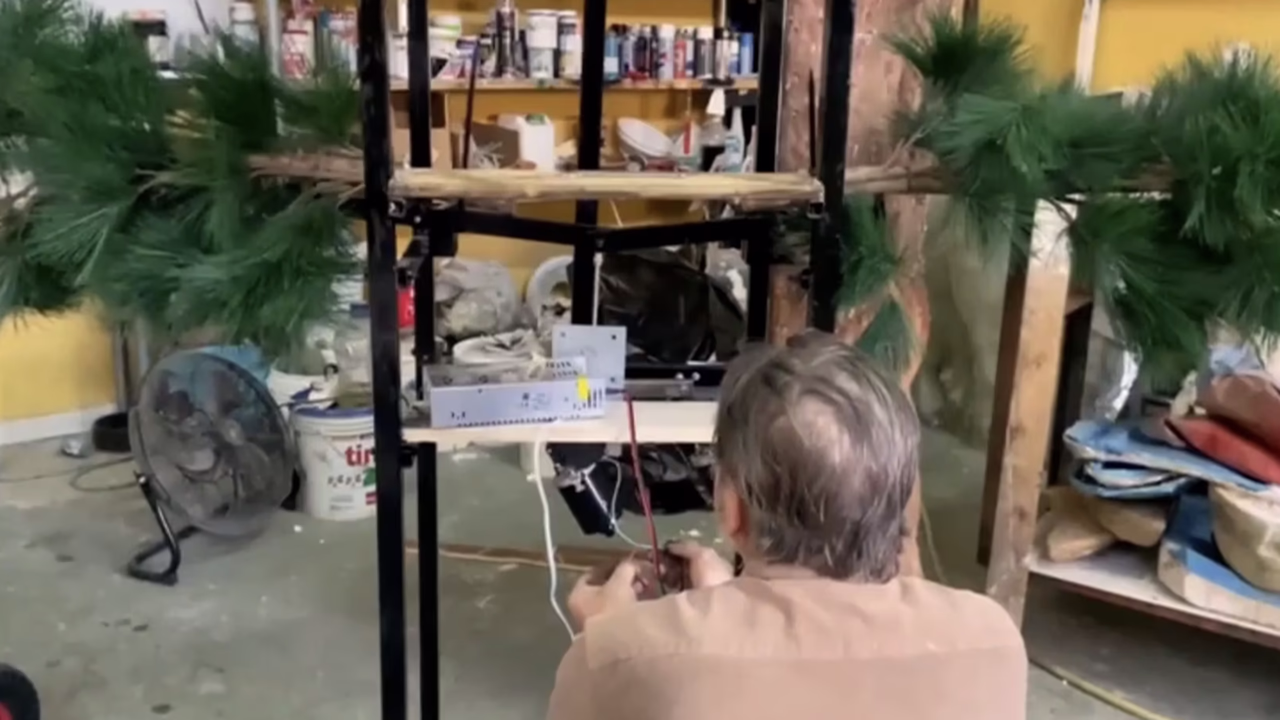 Menart artist at work in the scenographic laboratory, detailing decorative elements between artificial palm trees and materials, illustrating the company's artisanal creative process.