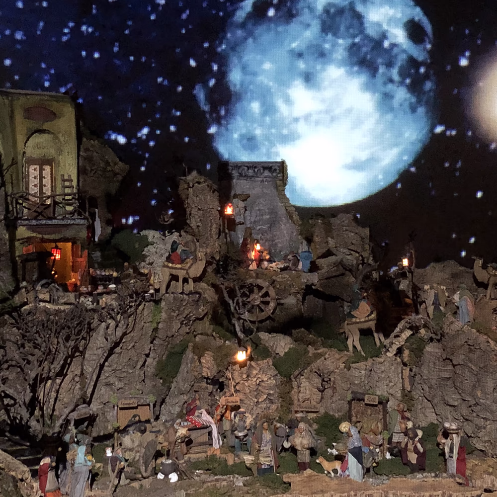 Presepe scenografico multimediale con architetture in pietra illuminata, proiezioni di cielo stellato e luna, creando atmosfera natalizia suggestiva per allestimento natalizio professionale.