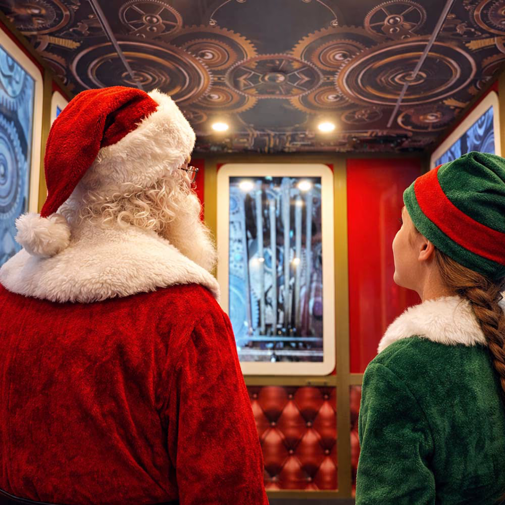 Babbo Natale e un elfo guardano l'interno decorato di un ascensore con ingranaggi sul soffitto.