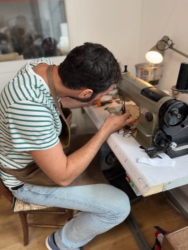Homme assis travaillant avec une machine à coudre industrielle sur une table dans un atelier.