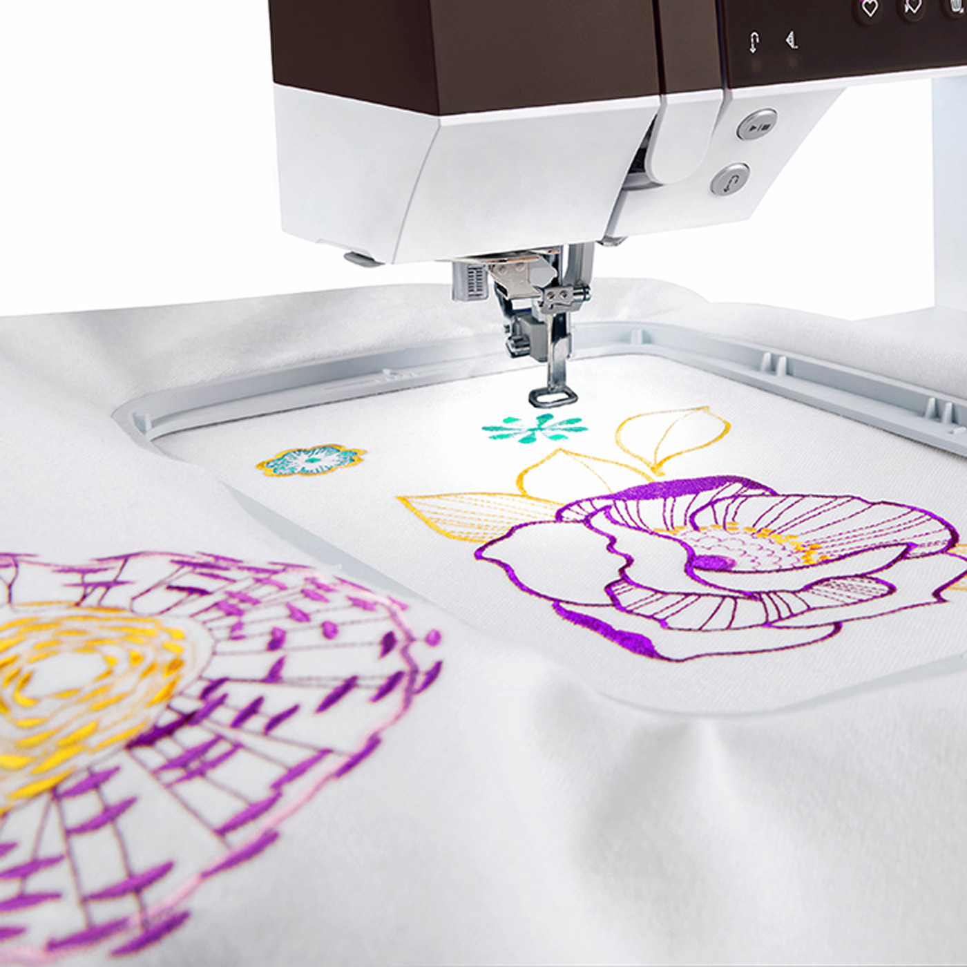 Machine à broder en cours de création d'un motif floral coloré sur un tissu blanc.