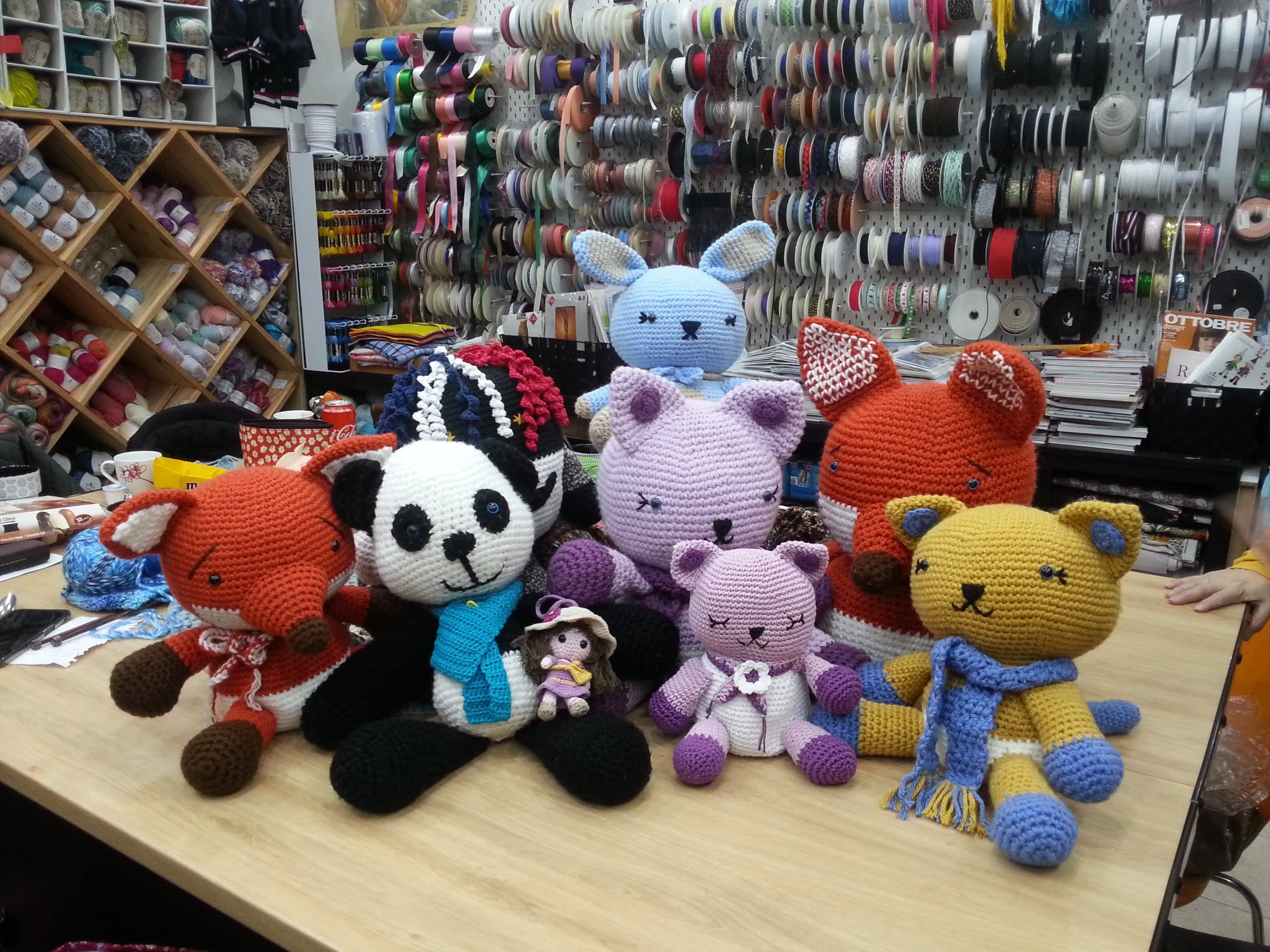 Peluches crochetées colorées sur une table dans un atelier rempli de fils et rubans.