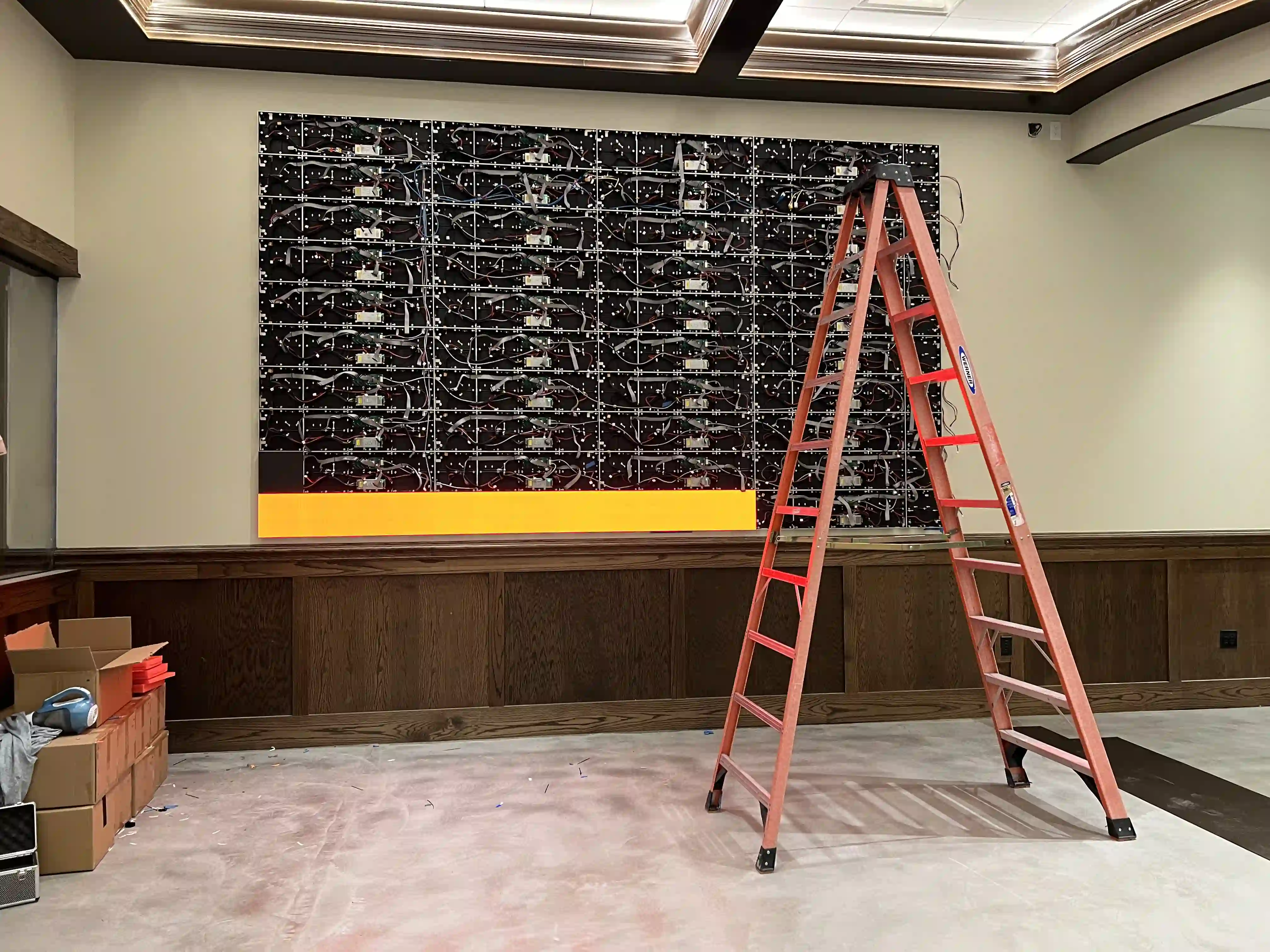 CMG Visuals installing LED video wall panels during a luxury lounge project, showing wiring and cabinet structure behind the display.